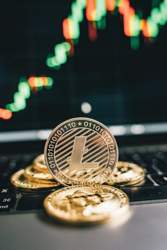 Gold Litecoin and Bitcoin coins on a laptop keyboard with a rising stock market chart in the background.